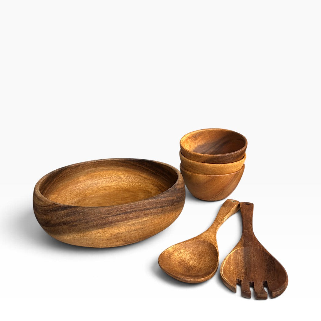 A wooden dining set including a large oval bowl, three small stacked bowls, a wooden spoon, and a wooden serving fork, all shown on a clean white background.