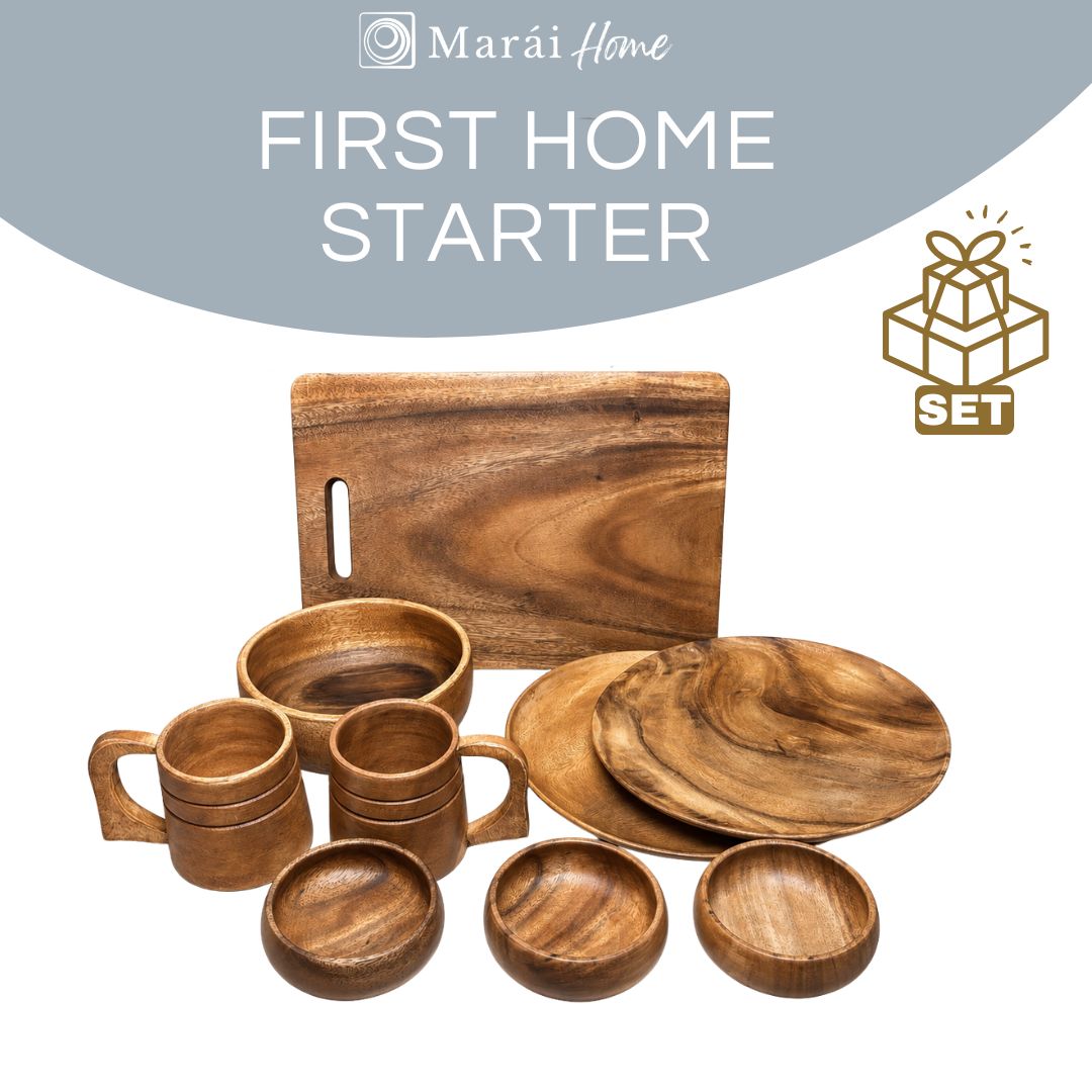 A wooden dining set displayed on a white background with a gray curved banner reading 'FIRST HOME STARTER' and a gift-set icon. The set includes a rectangular cutting board, two stacked mugs, two small mugs, two shallow bowls, two round plates, and two shallow round bowls, all in warm medium-brown wood tones.